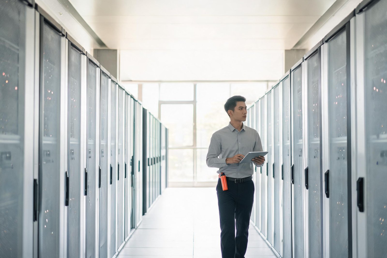 Technician walking through a bright data center corridor holding a tablet